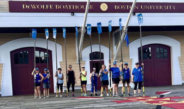 WeCanRow members holding their oars vertically in front of the BU DeWolfe Boathouse.